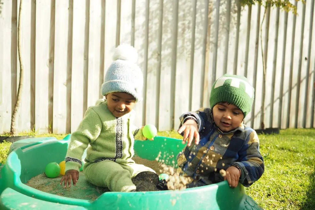Two toddlers exploring sand and balls outdoors